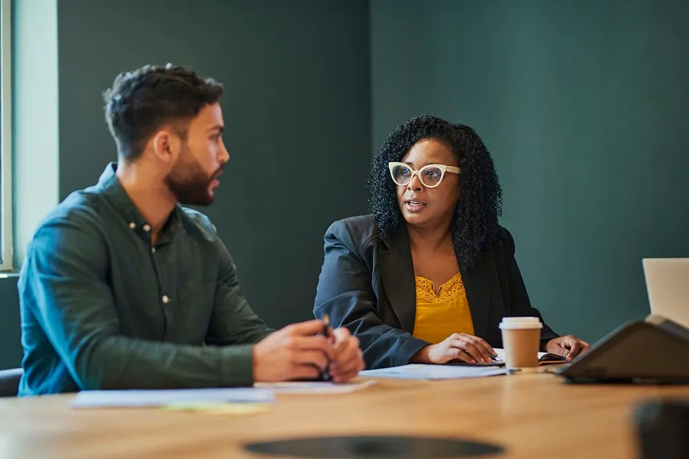 Two colleagues meeting at a conference table to discuss a workplace issue.